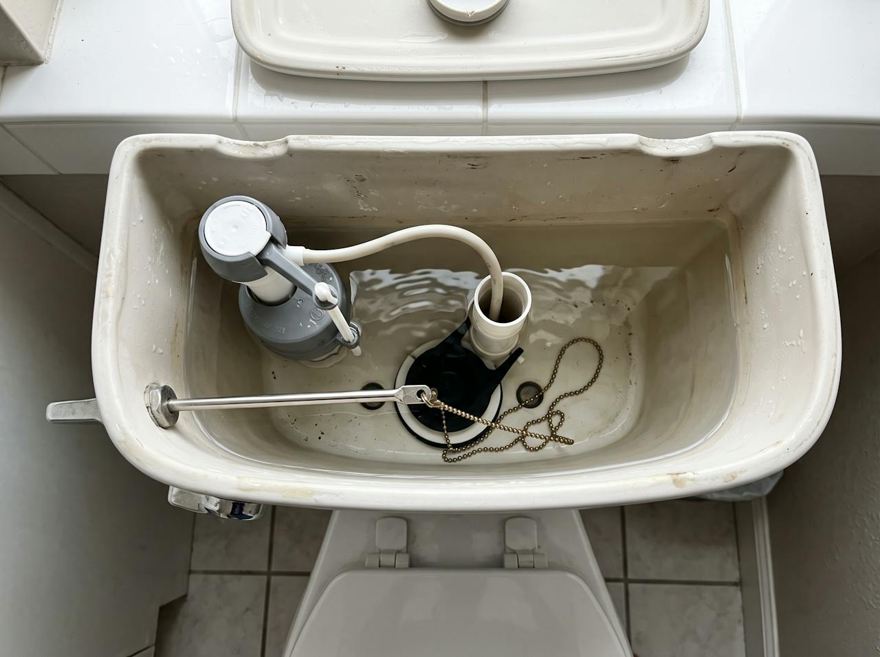 Open toilet tank with the flapper chain unhooked and lying loose in the water